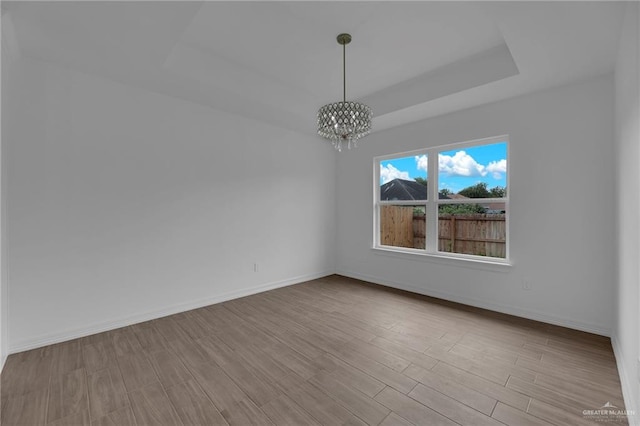 spare room with a chandelier, light hardwood / wood-style floors, and a raised ceiling