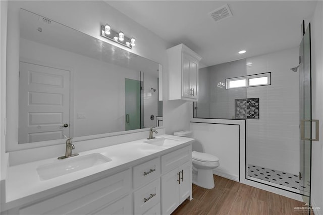 bathroom with a tile shower, vanity, wood-type flooring, and toilet