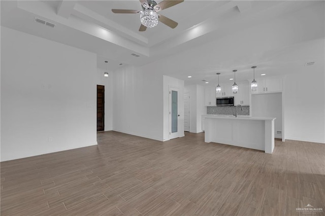 unfurnished living room featuring a tray ceiling, ceiling fan, sink, and light wood-type flooring