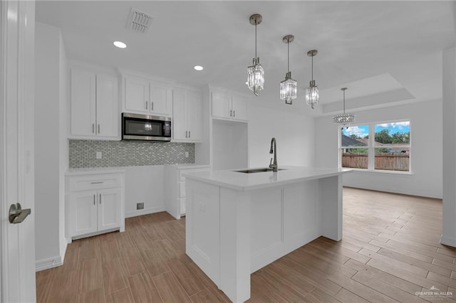 kitchen featuring light wood-type flooring, a kitchen island with sink, sink, decorative light fixtures, and white cabinetry