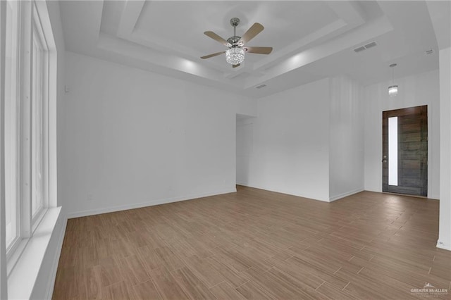 unfurnished room featuring a raised ceiling, ceiling fan, and light wood-type flooring