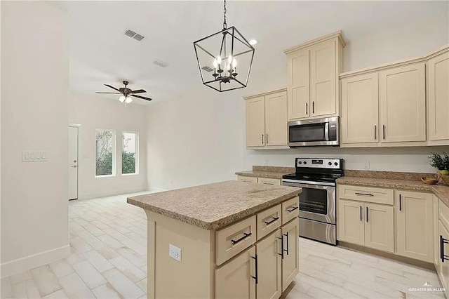 kitchen featuring pendant lighting, a kitchen island, cream cabinetry, appliances with stainless steel finishes, and ceiling fan with notable chandelier