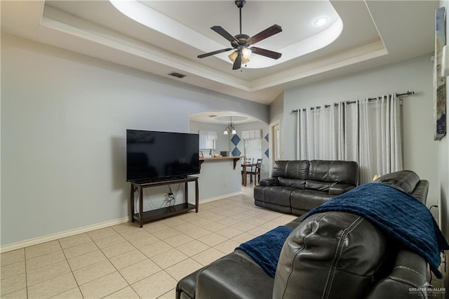 living area with arched walkways, light tile patterned floors, a ceiling fan, baseboards, and a tray ceiling