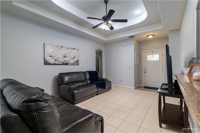 living room featuring arched walkways, ceiling fan, light tile patterned floors, baseboards, and a tray ceiling