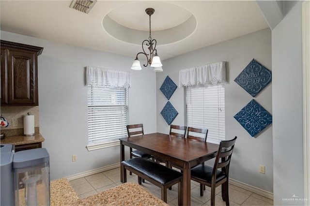 dining area featuring a tray ceiling, a notable chandelier, light tile patterned floors, visible vents, and baseboards