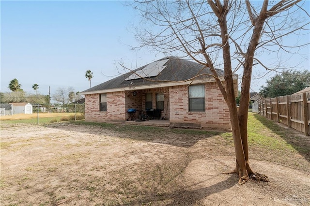 back of house with a shingled roof, fence, a patio area, roof mounted solar panels, and brick siding