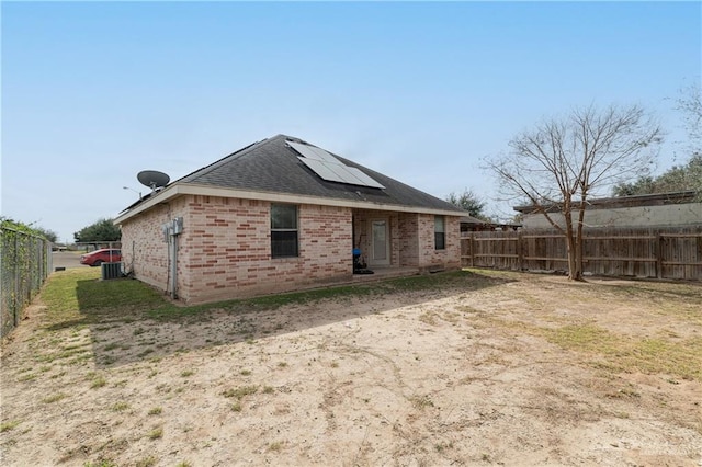 rear view of property with brick siding, solar panels, a shingled roof, central AC, and a fenced backyard