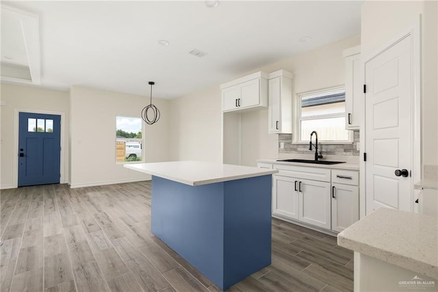 kitchen featuring white cabinets, a kitchen island, sink, and hanging light fixtures