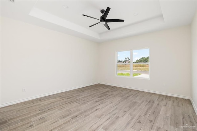 spare room with ceiling fan, a raised ceiling, and light wood-type flooring