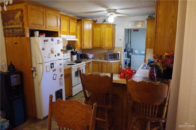 kitchen featuring white appliances, ceiling fan, a kitchen bar, washer / clothes dryer, and light tile patterned flooring