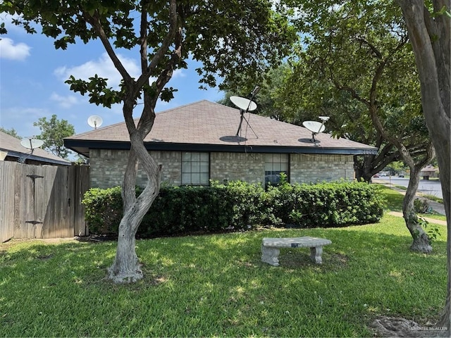exterior space with a lawn, fence, a shingled roof, and brick siding