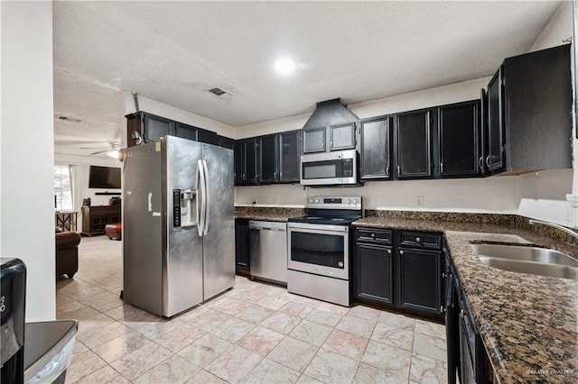 kitchen featuring sink, ceiling fan, appliances with stainless steel finishes, a textured ceiling, and dark stone counters