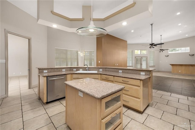 kitchen featuring dishwasher, light brown cabinetry, hanging light fixtures, and an island with sink