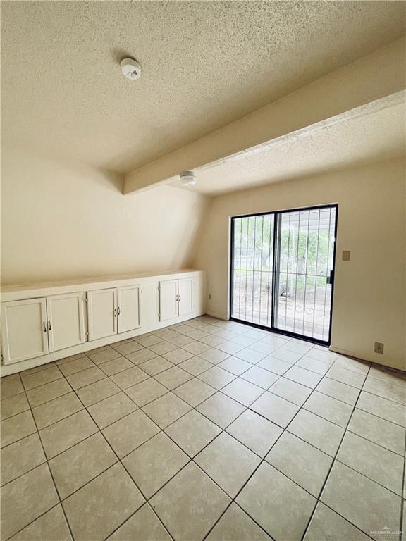 additional living space featuring vaulted ceiling with beams, light tile patterned floors, and a textured ceiling