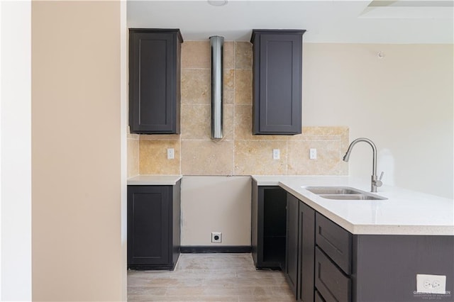 kitchen featuring tasteful backsplash, a peninsula, light countertops, light wood-type flooring, and a sink