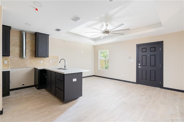 kitchen featuring light wood finished floors, a raised ceiling, visible vents, a sink, and a peninsula