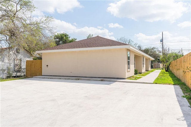 view of home's exterior with a shingled roof, fence, and stucco siding