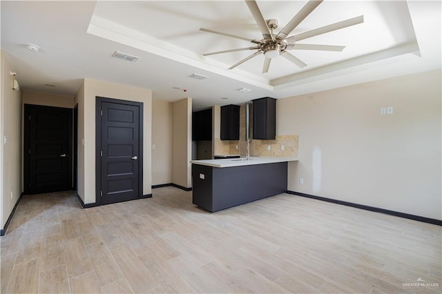 kitchen with a tray ceiling, light countertops, visible vents, light wood-style flooring, and a peninsula