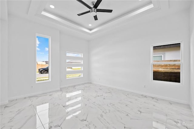 empty room featuring a raised ceiling, marble finish floor, and baseboards