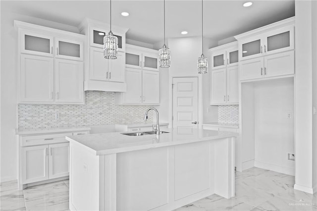 kitchen with marble finish floor, a center island with sink, light countertops, glass insert cabinets, and white cabinets