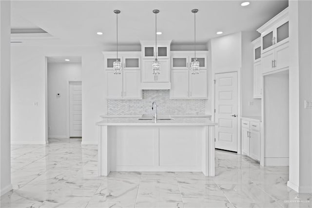 kitchen featuring an island with sink, glass insert cabinets, light countertops, and pendant lighting