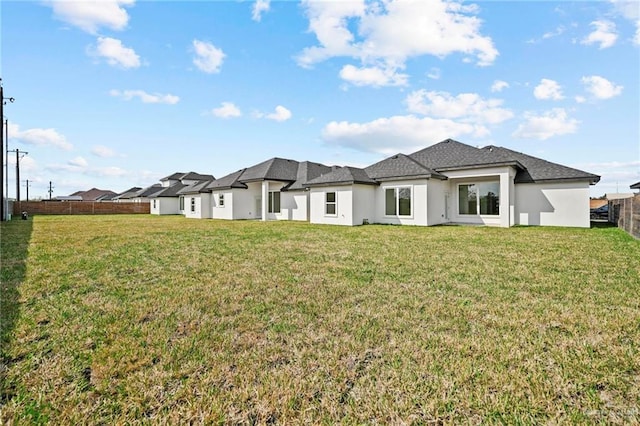 back of house with a lawn, fence, and stucco siding