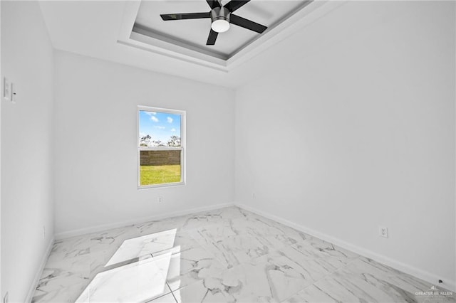 spare room featuring marble finish floor, baseboards, a tray ceiling, and ceiling fan