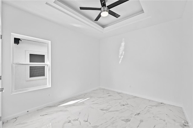 spare room with marble finish floor, a raised ceiling, and baseboards