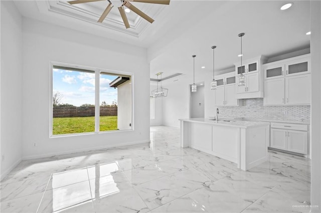 kitchen featuring a center island with sink, light countertops, hanging light fixtures, glass insert cabinets, and white cabinets