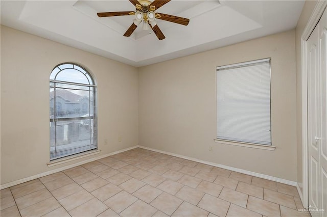 tiled empty room featuring ceiling fan and a raised ceiling