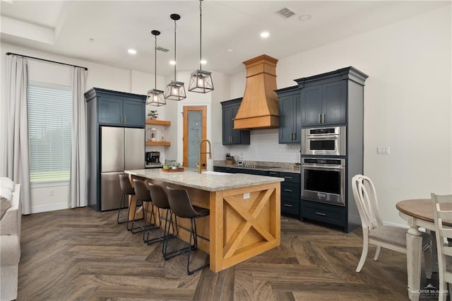 3524 Inez St, Edinburg, TX 78539 - kitchen featuring appliances with stainless steel finishes, open shelves, custom range hood, decorative backsplash, and a kitchen island with sink