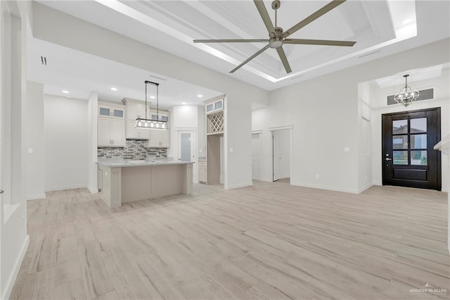 1007 Broken Arrow Dr, Alamo, TX 78516 - unfurnished living room featuring light wood finished floors, a tray ceiling, baseboards, and ceiling fan with notable chandelier