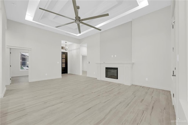 1007 Broken Arrow Dr, Alamo, TX 78516 - unfurnished living room with ceiling fan with notable chandelier, a tray ceiling, light wood finished floors, and a glass covered fireplace
