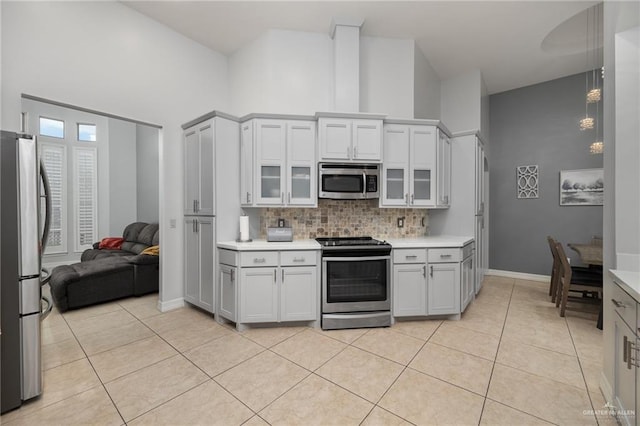 kitchen featuring decorative backsplash, a towering ceiling, stainless steel appliances, light tile patterned floors, and white cabinets