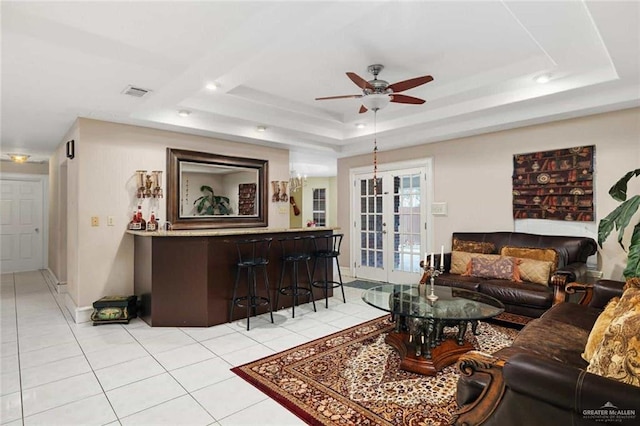 tiled living room with a raised ceiling, ceiling fan, and french doors