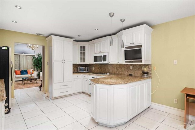 kitchen featuring pendant lighting, kitchen peninsula, stainless steel fridge, tasteful backsplash, and white cabinetry