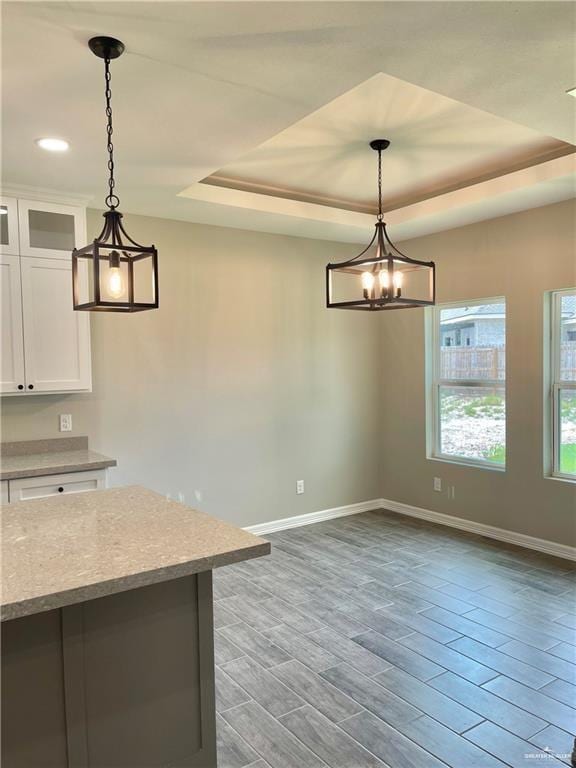 kitchen with light stone counters, wood-type flooring, hanging light fixtures, a tray ceiling, and white cabinets