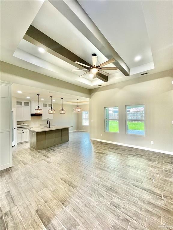 unfurnished living room featuring sink, a tray ceiling, and ceiling fan