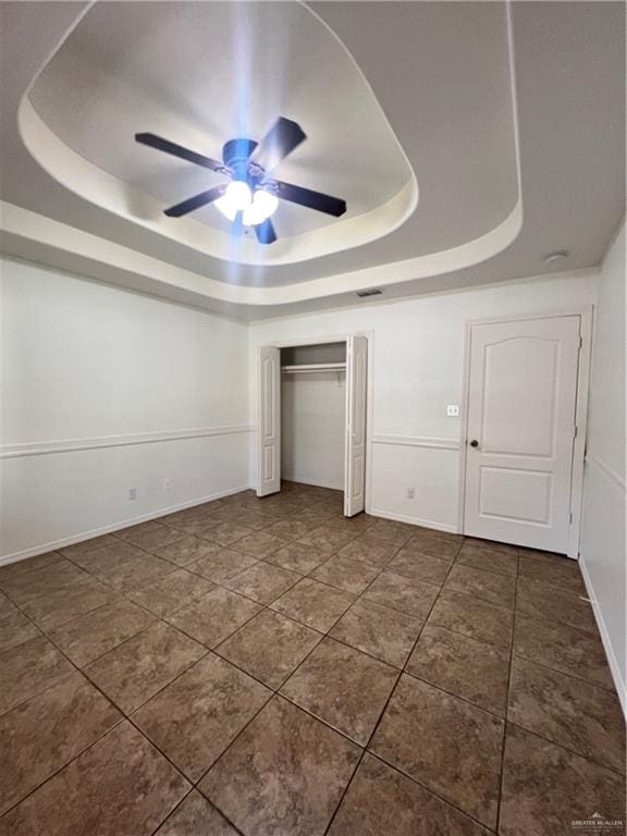 unfurnished bedroom featuring a tray ceiling, ceiling fan, a closet, and dark tile patterned flooring