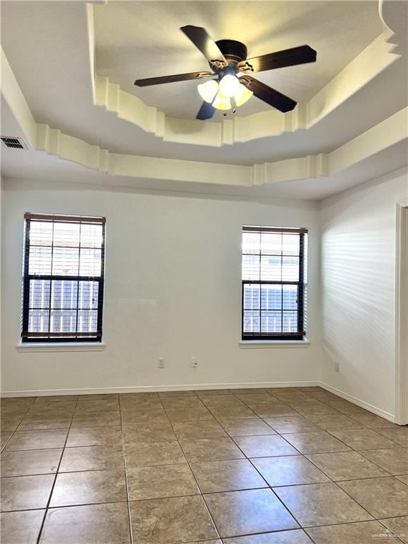 tiled empty room featuring a raised ceiling and ceiling fan