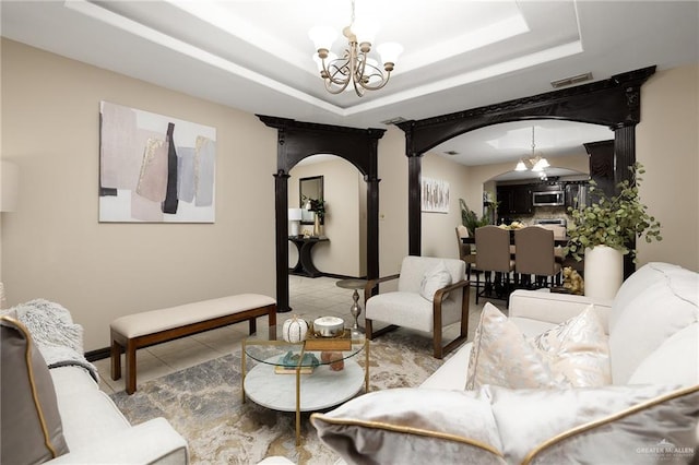 living room featuring tile patterned flooring, a raised ceiling, and an inviting chandelier