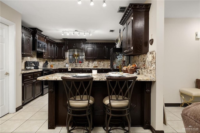 kitchen featuring a breakfast bar, dark brown cabinets, black range, and light tile patterned floors