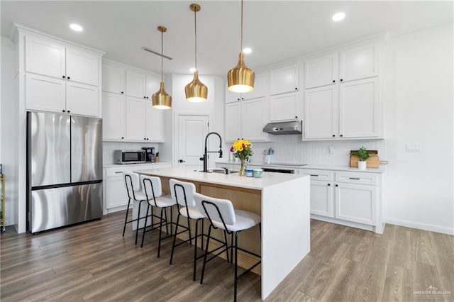 7423 Converse Lk, Brownsville, TX 78520 - kitchen featuring appliances with stainless steel finishes, decorative backsplash, wood finished floors, white cabinets, and an island with sink