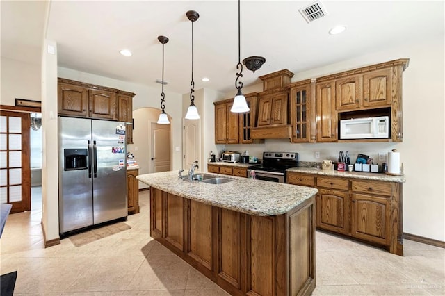 2017 Stonebriar Rd, Harlingen, TX 78552 - kitchen featuring appliances with stainless steel finishes, an island with sink, brown cabinetry, glass insert cabinets, and pendant lighting