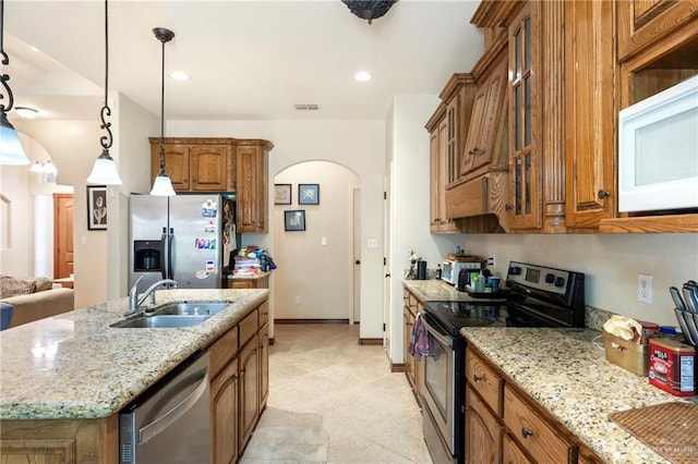 2017 Stonebriar Rd, Harlingen, TX 78552 - kitchen with stainless steel appliances, arched walkways, brown cabinetry, a center island with sink, and light stone countertops
