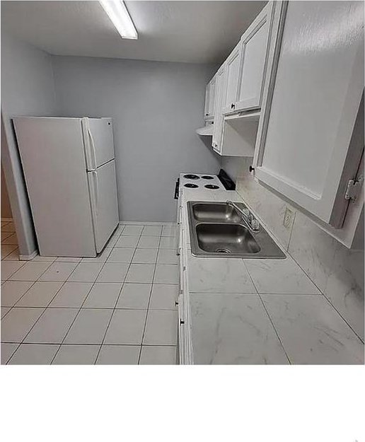 kitchen featuring tile countertops, extractor fan, a sink, white cabinets, and freestanding refrigerator