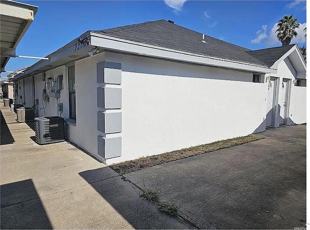 view of side of property featuring roof with shingles, central air condition unit, and stucco siding