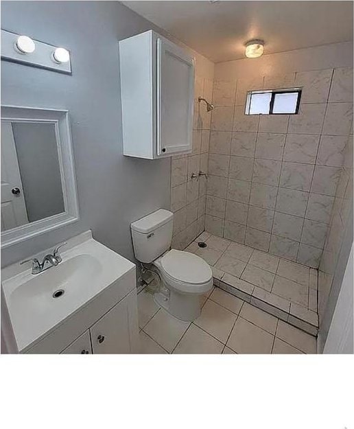 full bath featuring a tile shower, vanity, and toilet