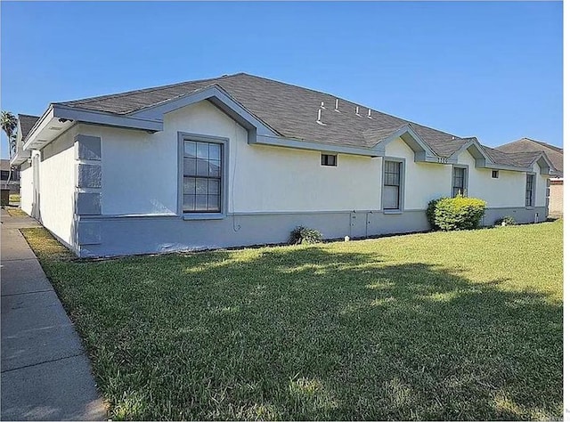 view of home's exterior with a yard, a shingled roof, and stucco siding