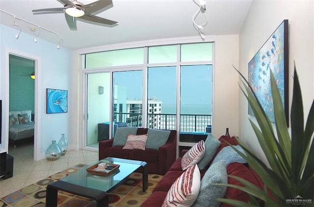 tiled living area with rail lighting, a wall of windows, ceiling fan, and a water view